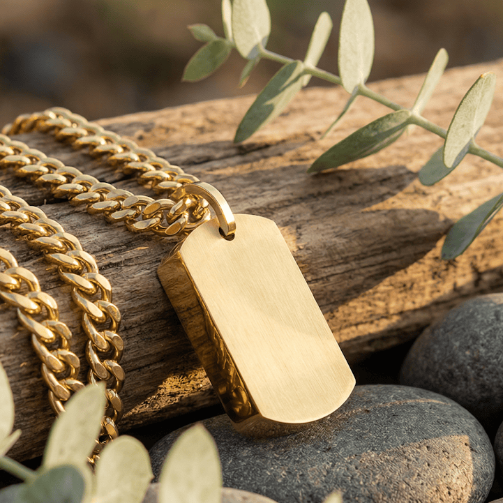 Gold necklace with a tag on a wooden log and pebbles with greenery